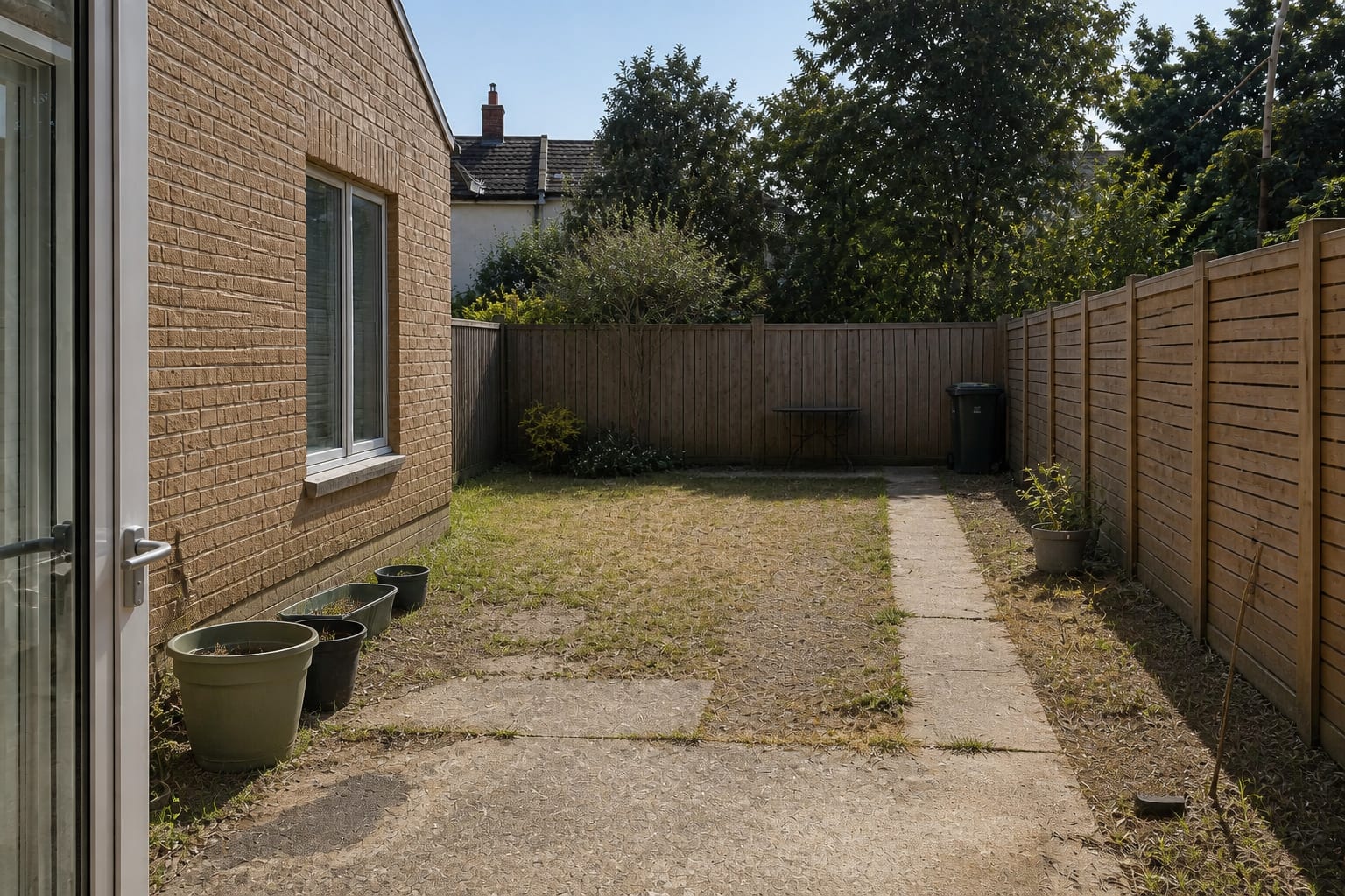 Patchy lawn garden with scattered plastic pots, exposed fencing, no shade, and an unused corner beside a narrow concrete path.