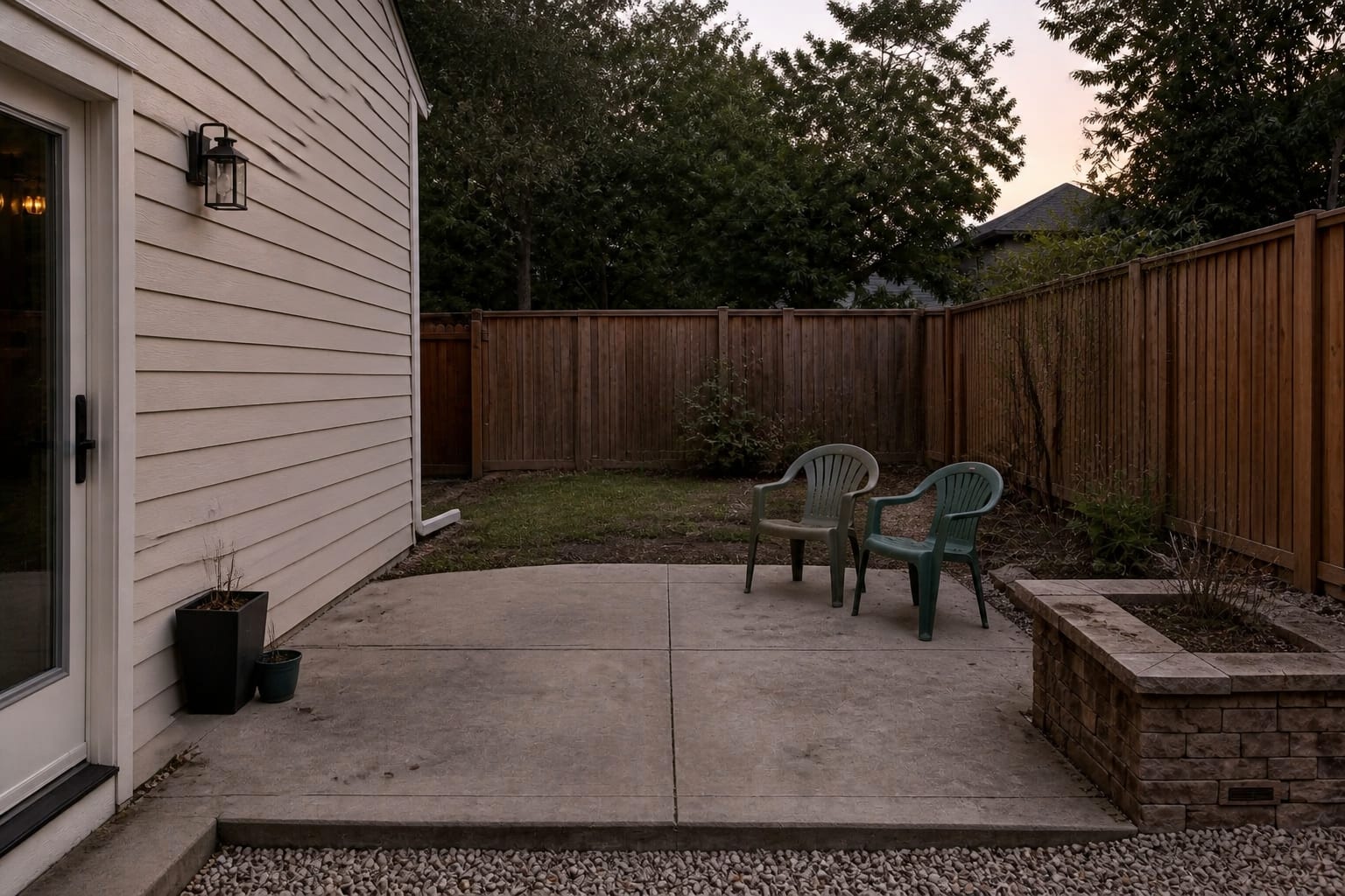 under-designed concrete patio with small scattered chairs, exposed siding, no shade, no rug, and a few undersized pots near the door.