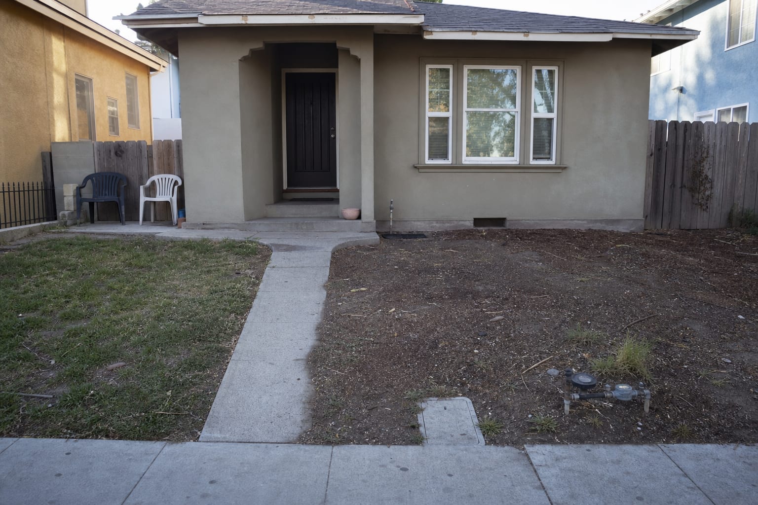 narrow townhouse front yard with patchy grass, a cramped concrete walk, exposed soil, and no clear planting structure