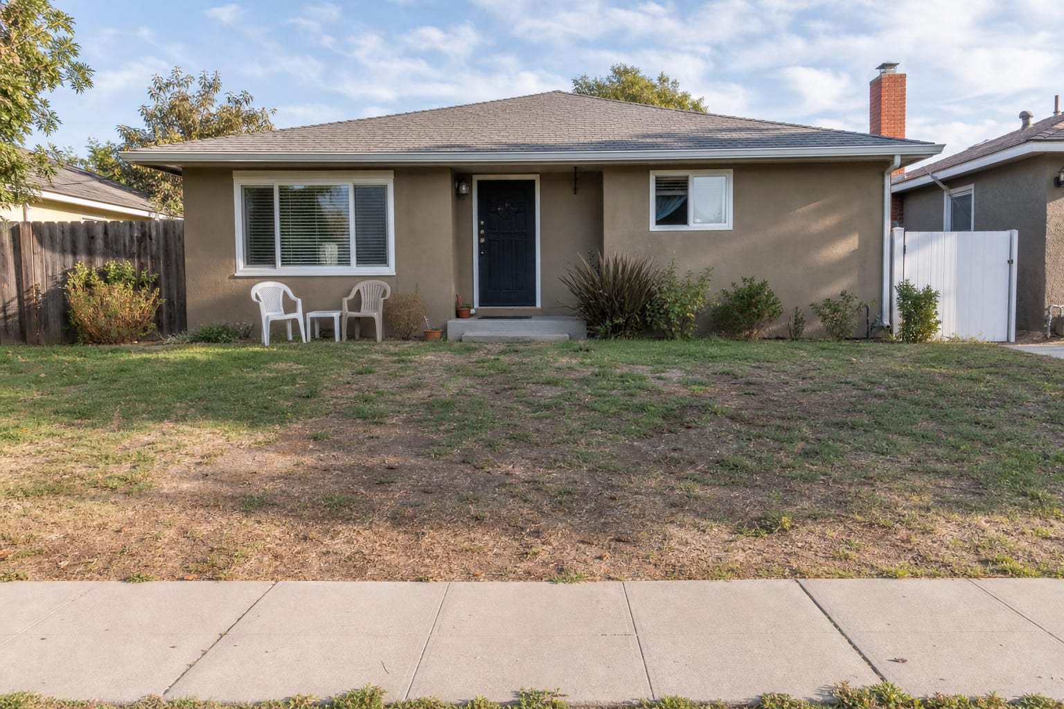 Patchy suburban front yard with narrow foundation planting, exposed mulch, isolated shrubs, and no clear path through the lawn.