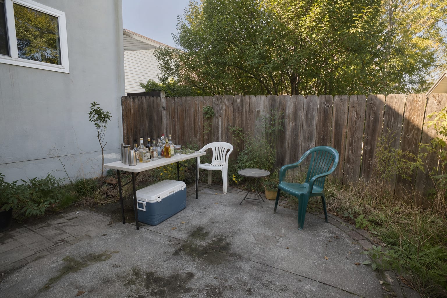 unplanned patio corner with a folding table, mismatched coolers, exposed fence, and no shade or serving counter