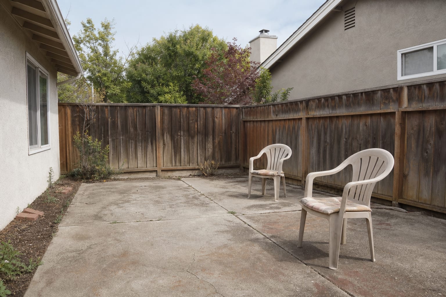 Bare patio chairs with thin faded cushions on concrete, no side table, and a seating area that looks unused.
