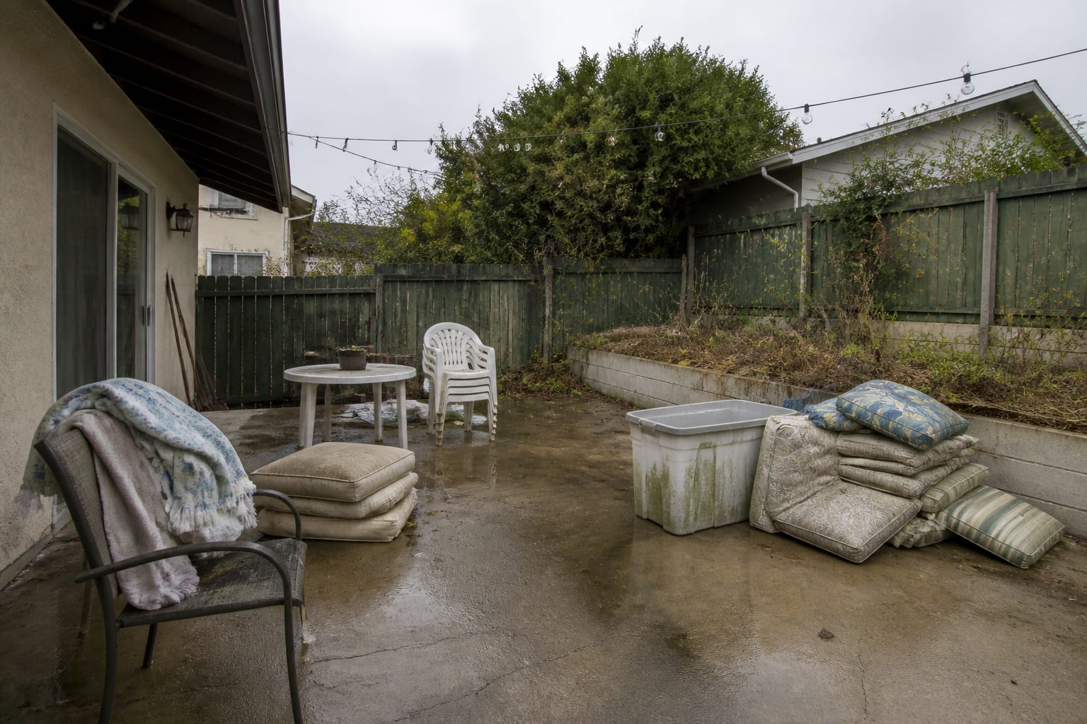 Patio with damp cushions piled on wet ground and a sealed bin growing mildew before redesign