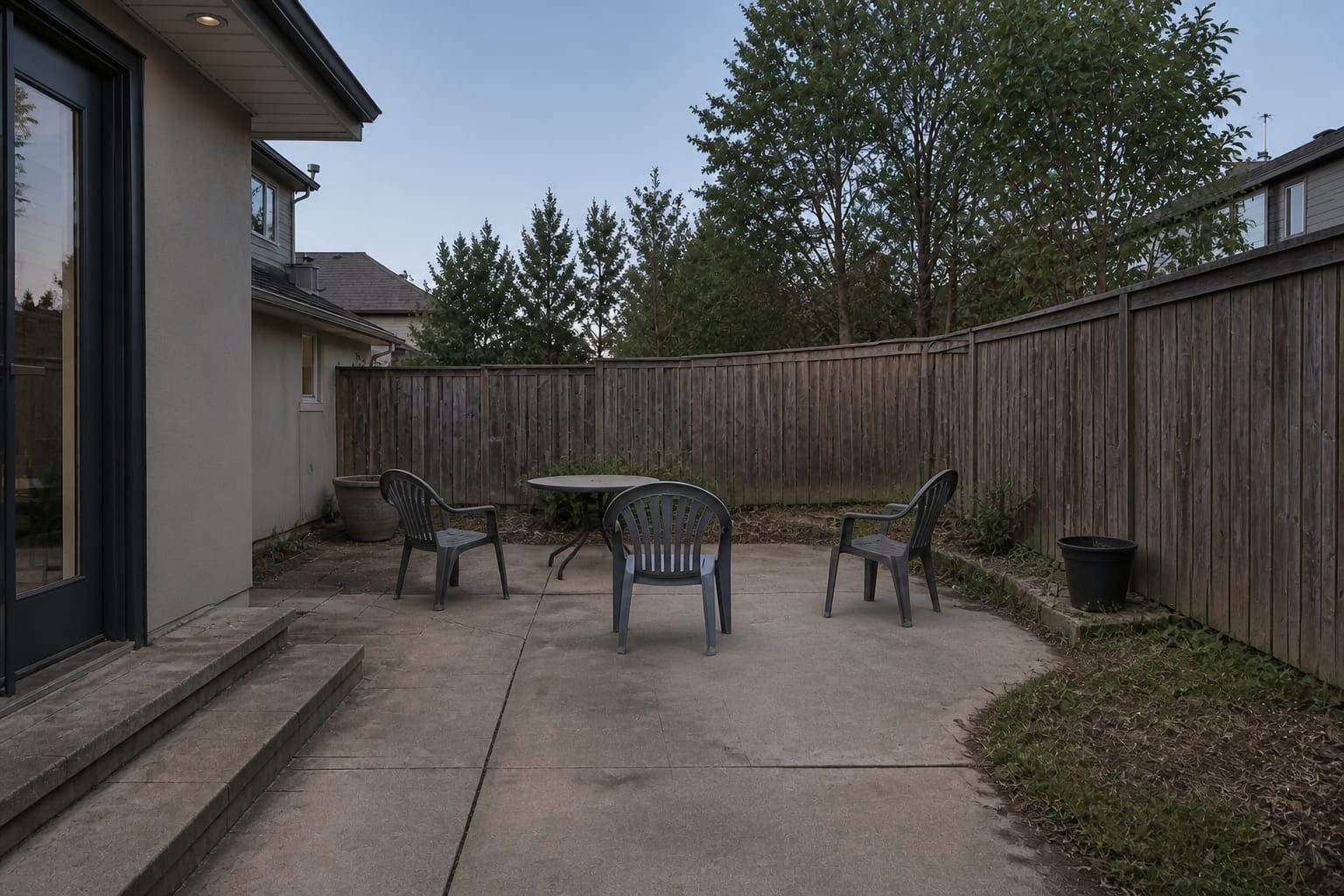 narrow patio with loose chairs, a blank stucco wall, cold concrete flooring, and no warm focal point for evening seating