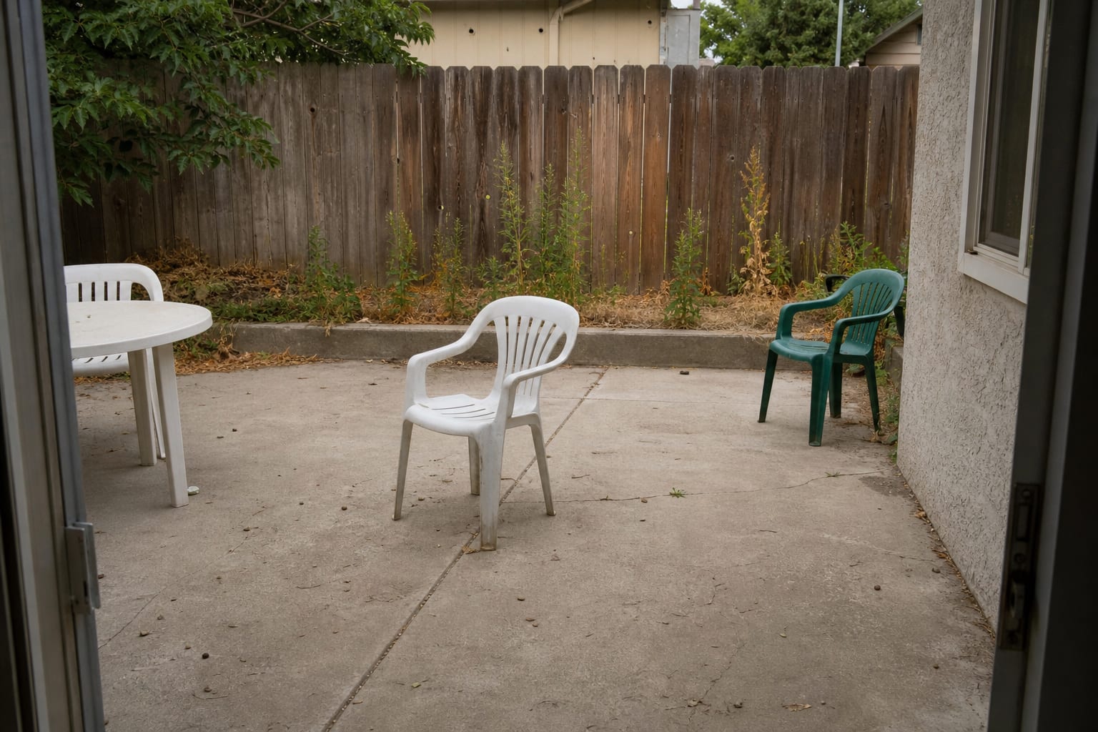 narrow patio with loose chairs, a blank stucco wall, cold concrete flooring, and no warm focal point for evening seating