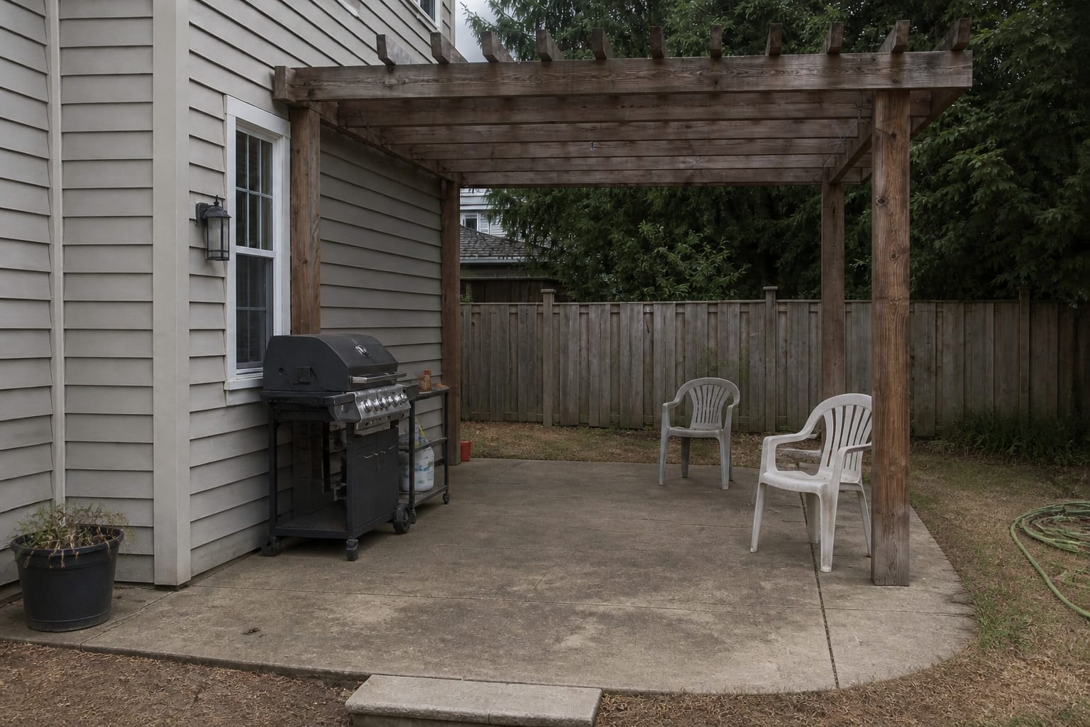 Patio grill area with a small metal cart, no real counter space, mismatched chairs, exposed tools, and a bare concrete slab.
