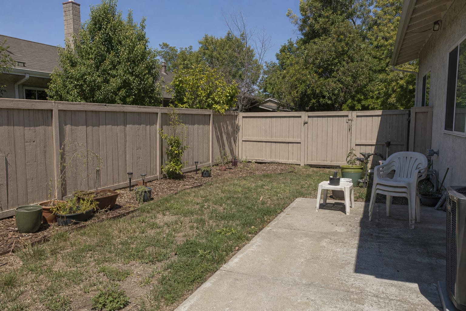 plain backyard corner with patchy lawn, exposed fence, random pots, and no comfortable place to sit quietly.