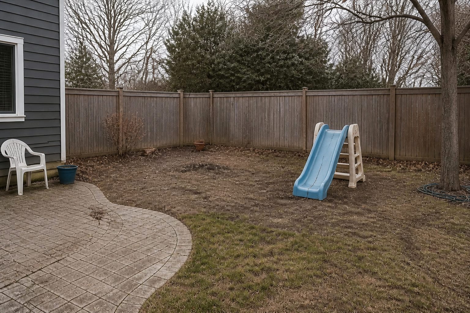 Empty patchy backyard corner with a faded cracked plastic toddler slide before a play area redesign
