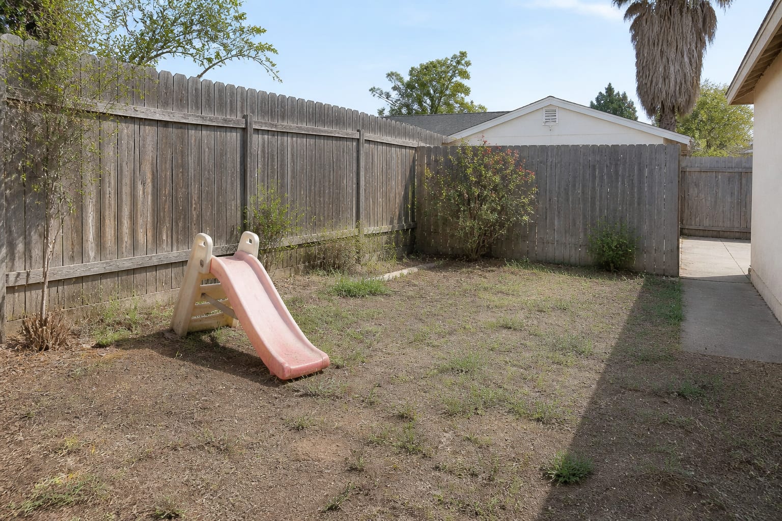 Empty patchy backyard corner with a faded cracked plastic toddler slide before a play area redesign