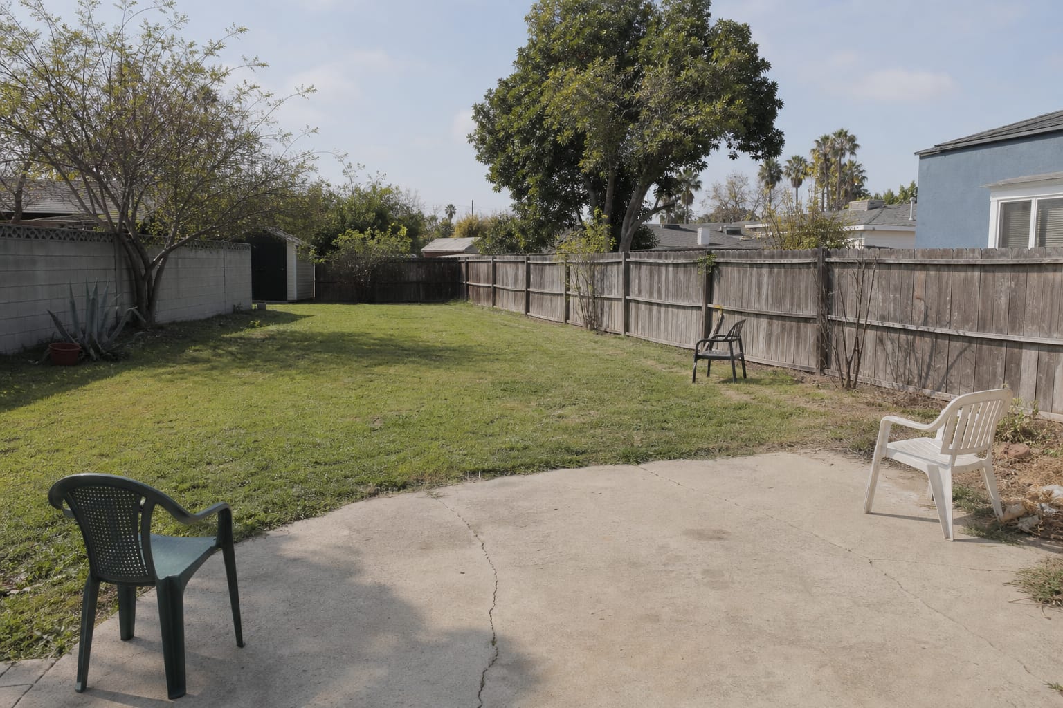 Open backyard with a large plain lawn, scattered chairs, exposed fence lines, and no defined dining or lounge zones.