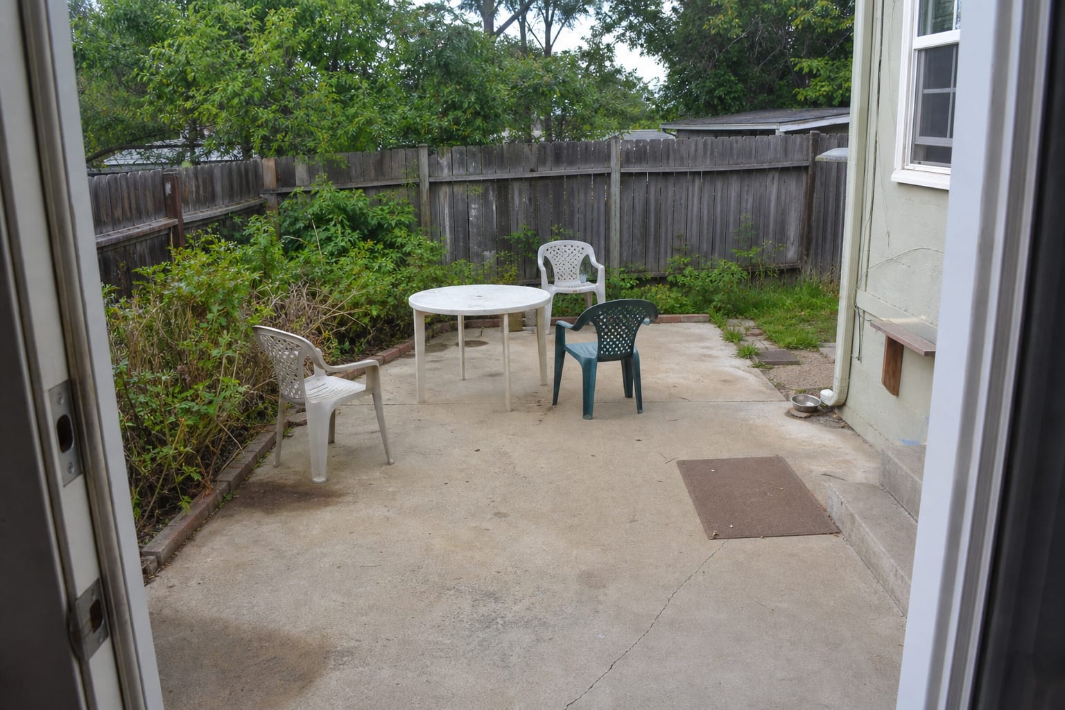 uncovered concrete patio with scattered chairs, a small side table, bare floor, and no visual boundary for the seating area.