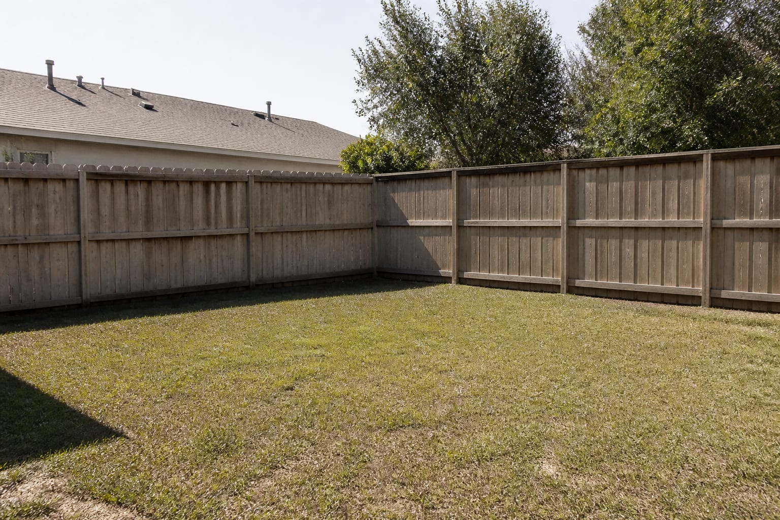 Empty backyard corner with patchy lawn and no focal point