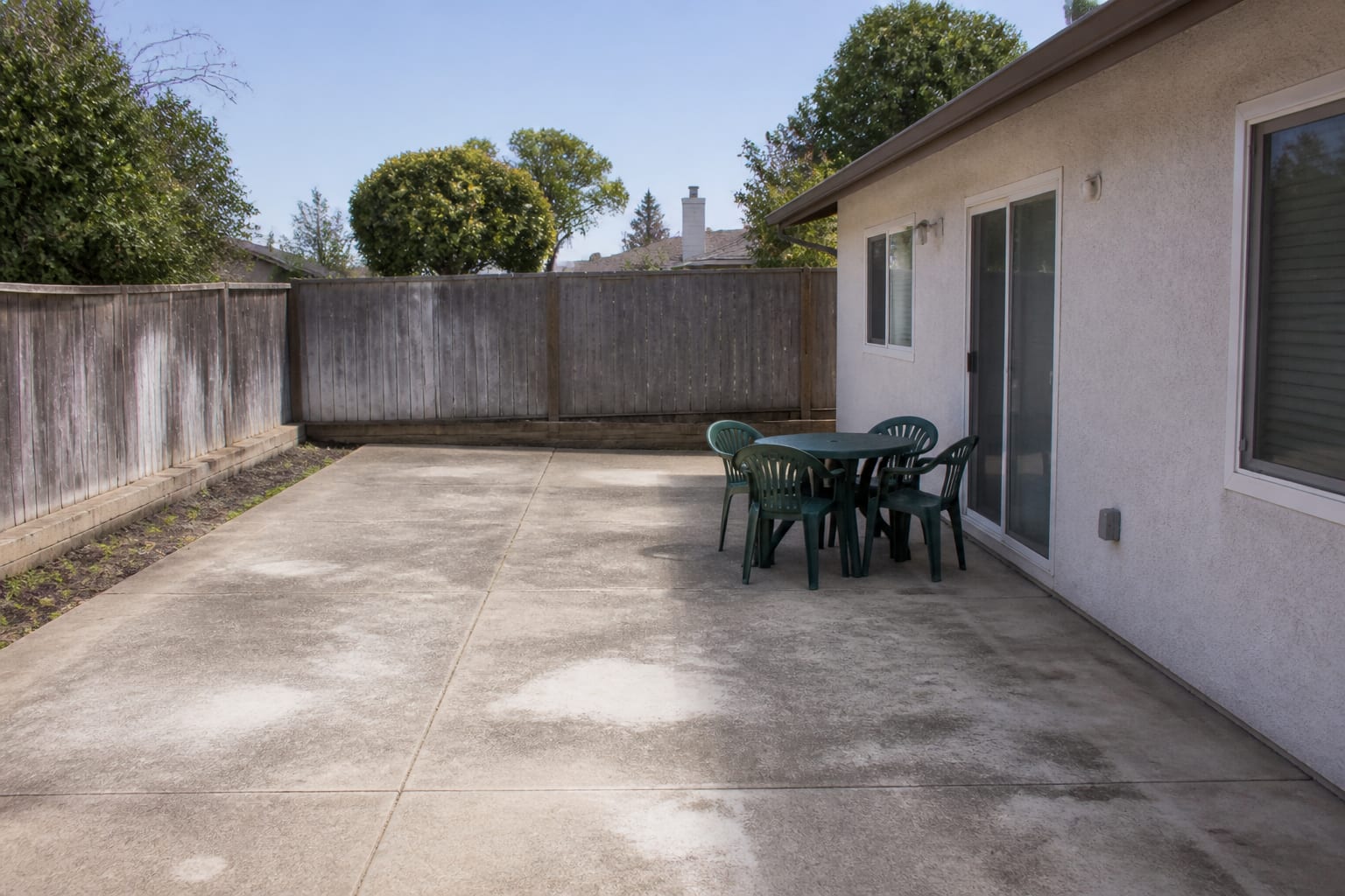 Bare concrete patio with a single stiff four-chair patio set and no rug, shade, or defined seating zone before redesign