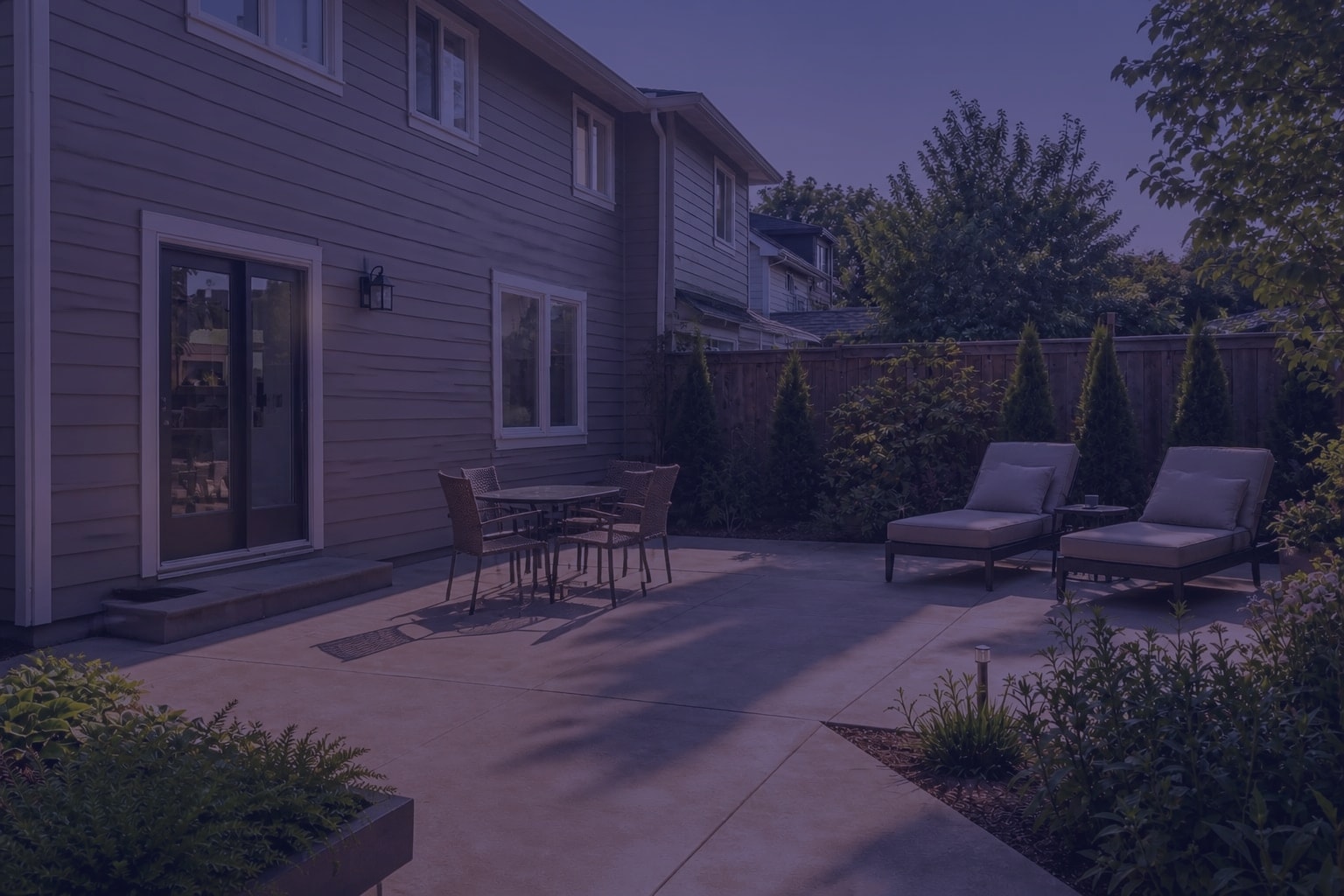 concrete patio with a small table, uncovered lounge chairs, strong afternoon glare, and no shade over the door or seating