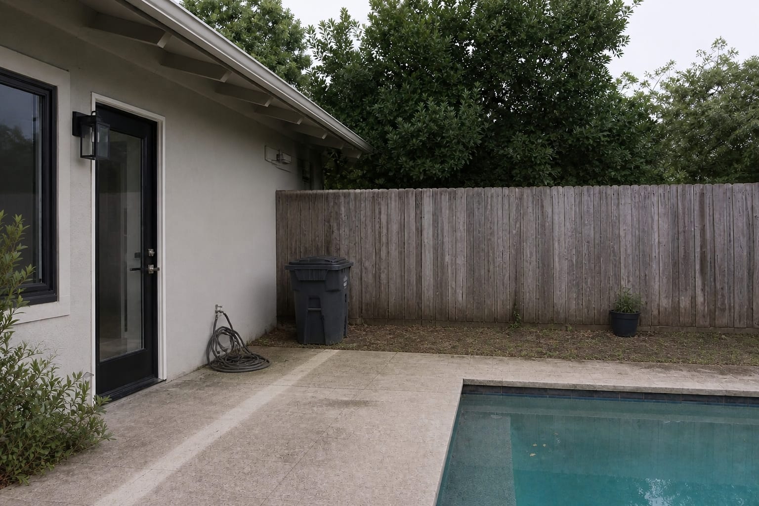 Poolside concrete corner with muddy towel pile, hose on the ground, bare fence, and no place to rinse before entering the house