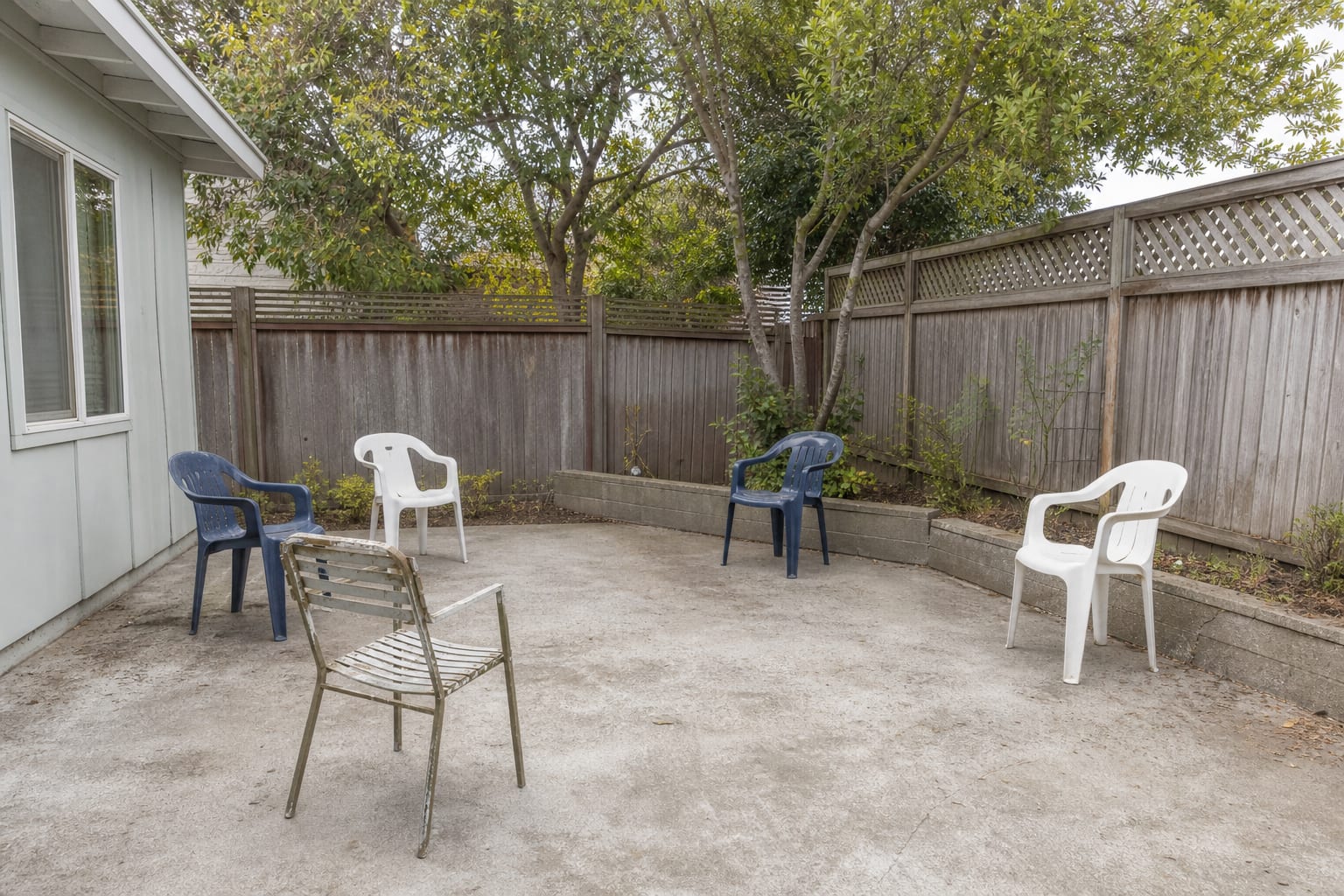 Bare patio corner with scattered outdoor chairs, no sofa, no shade, and no usable side surfaces for drinks or books.