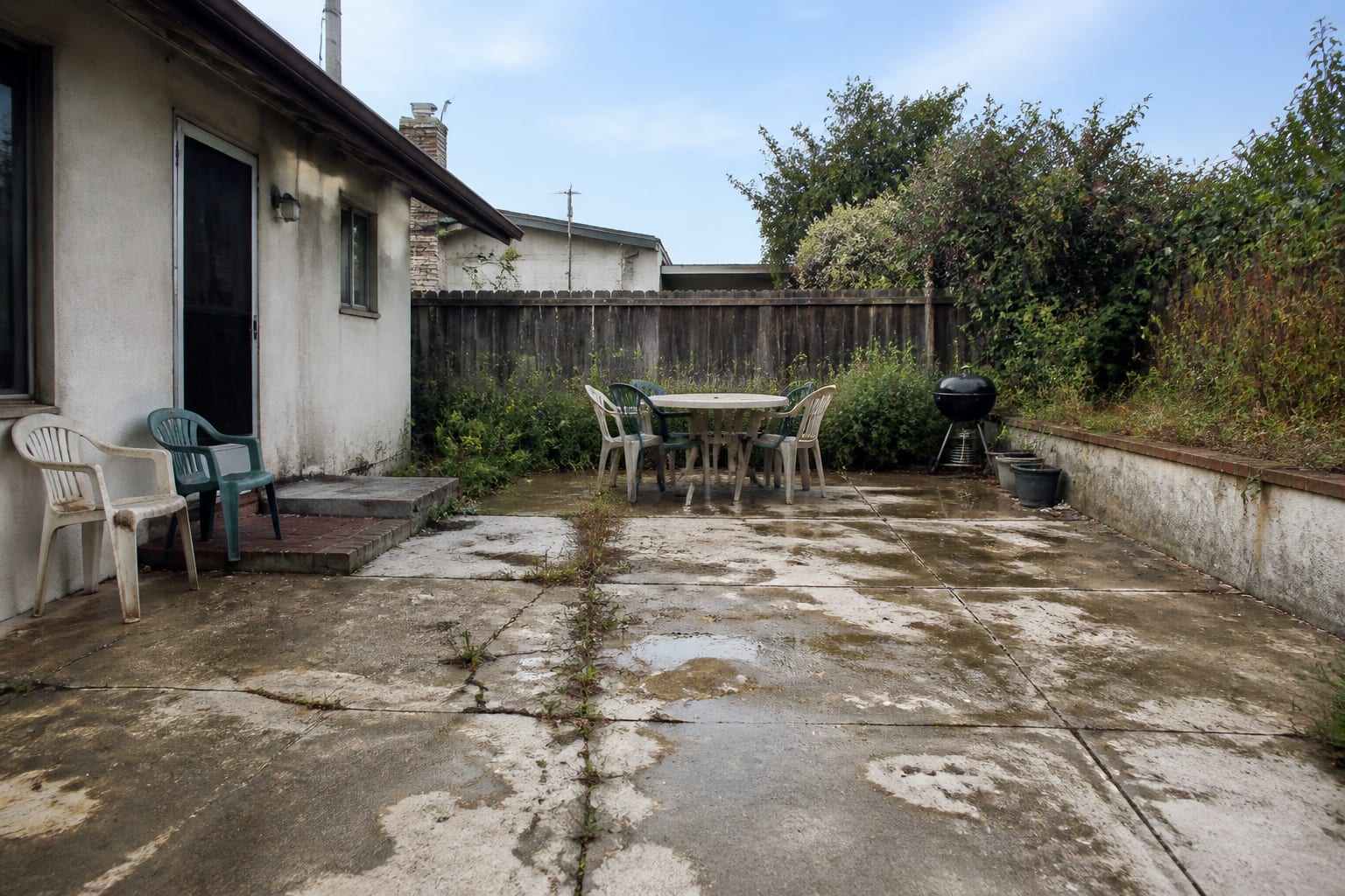 Cracked stained concrete patio with weeds in the joints and a slick polished surface before retiling
