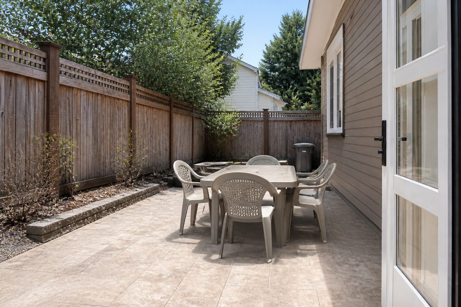 uncovered patio dining set on pale pavers with harsh midday glare, undersized umbrella base, and chairs crowded near the door