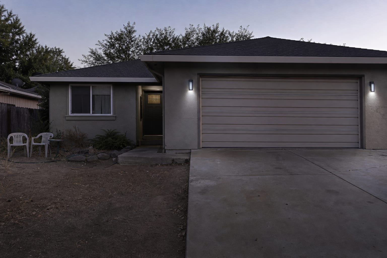 front exterior with undersized cool-white porch lights beside the door and garage, leaving the facade patchy after dusk.