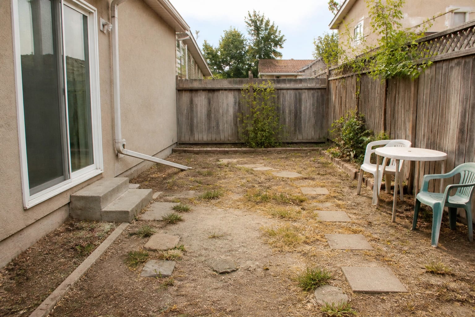 Bare dirt and patchy grass backyard area before a patio is installed