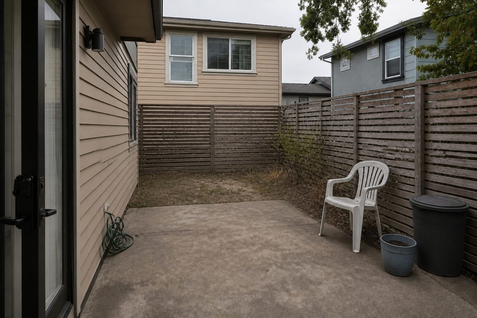 Exposed patio with low furniture, open fence gaps, bare concrete, and direct views from nearby neighbor windows.