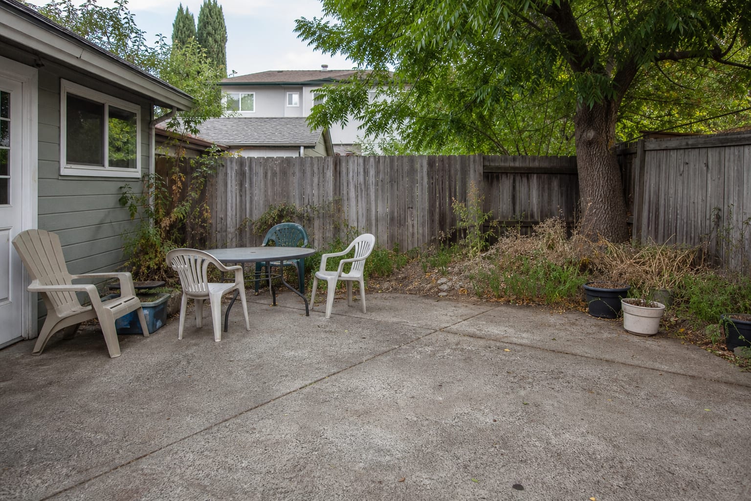 bare patio at dusk with scattered chairs, a dark dining table, no overhead lighting, and an undefined route from the house to the yard.