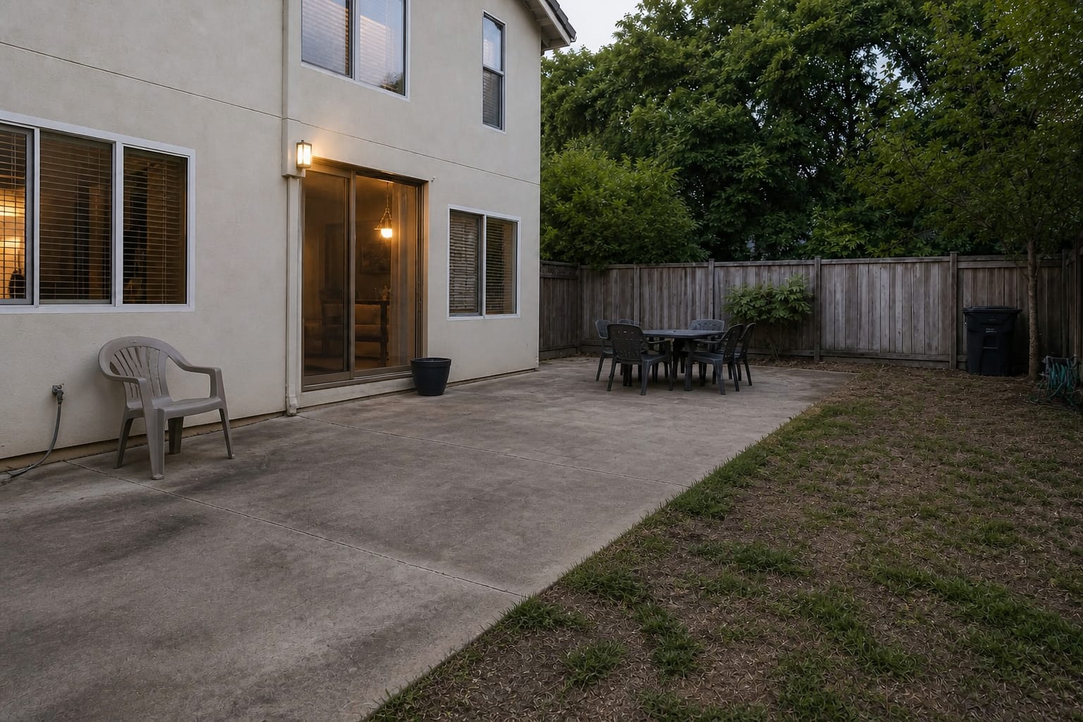 plain concrete patio ending abruptly at uneven grass with exposed soil and no border between the hardscape and lawn
