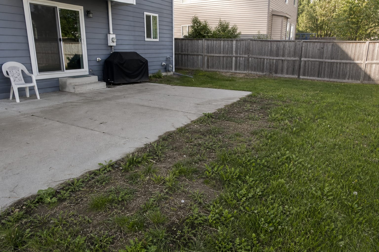 plain concrete patio ending abruptly at uneven grass with exposed soil and no border between the hardscape and lawn