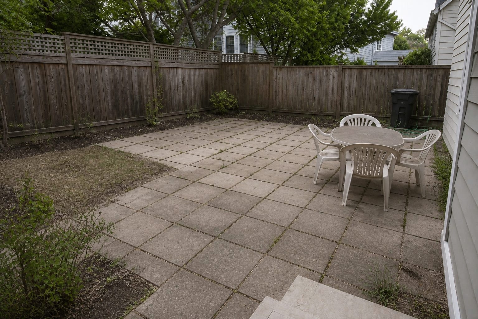 plain backyard patio with mismatched pavers, weeds in the joints, exposed edges, and no defined seating zone