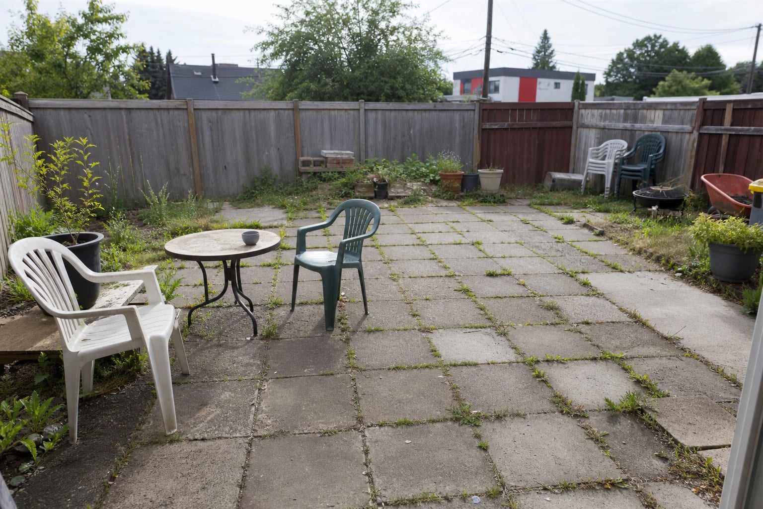 Plain concrete slab patio with scattered chairs, no border, and patchy lawn edges beside a small brick house.