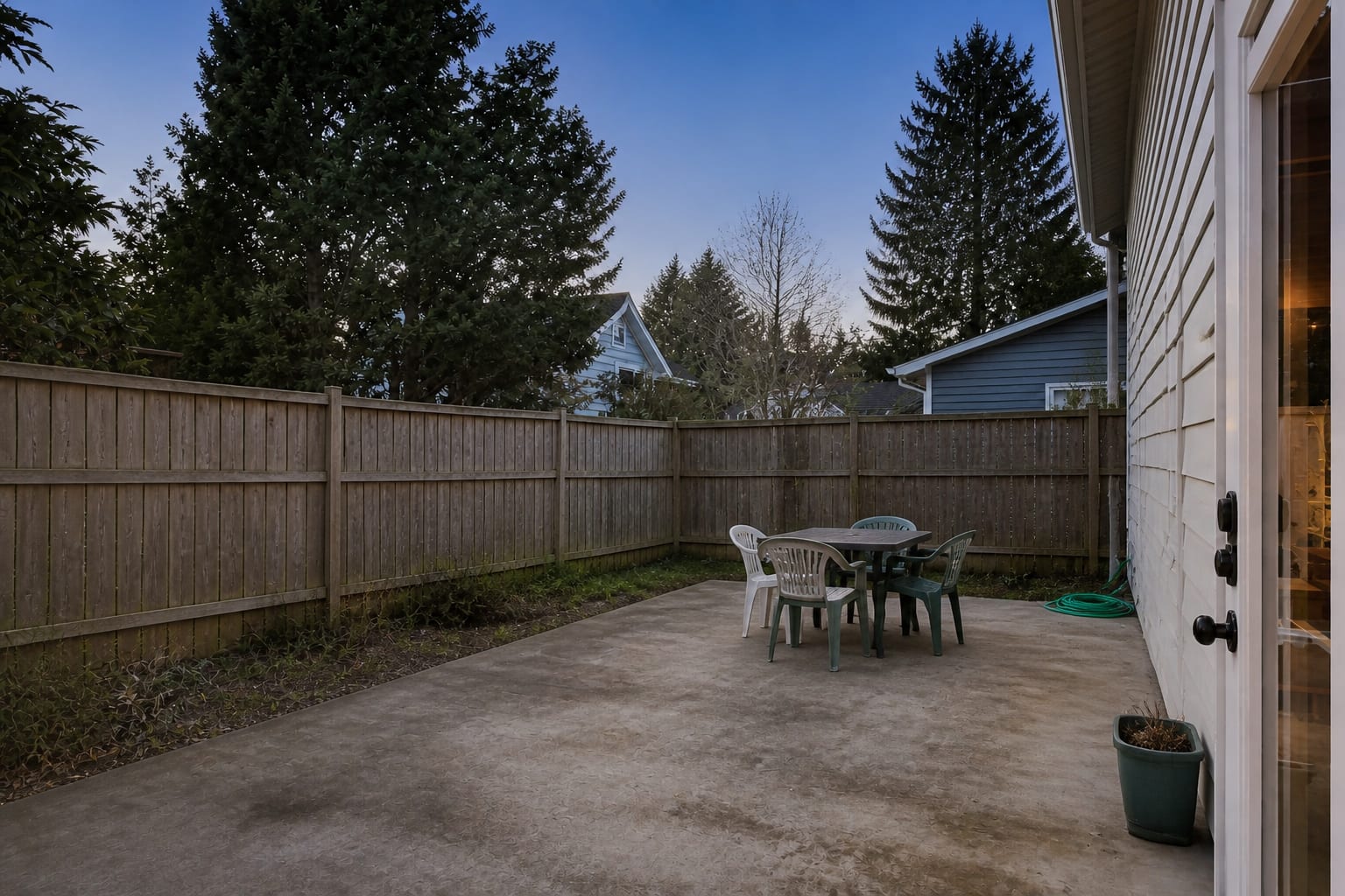 plain concrete patio with a small outdoor table, exposed fence line, and no shade structure or planting around the seating area