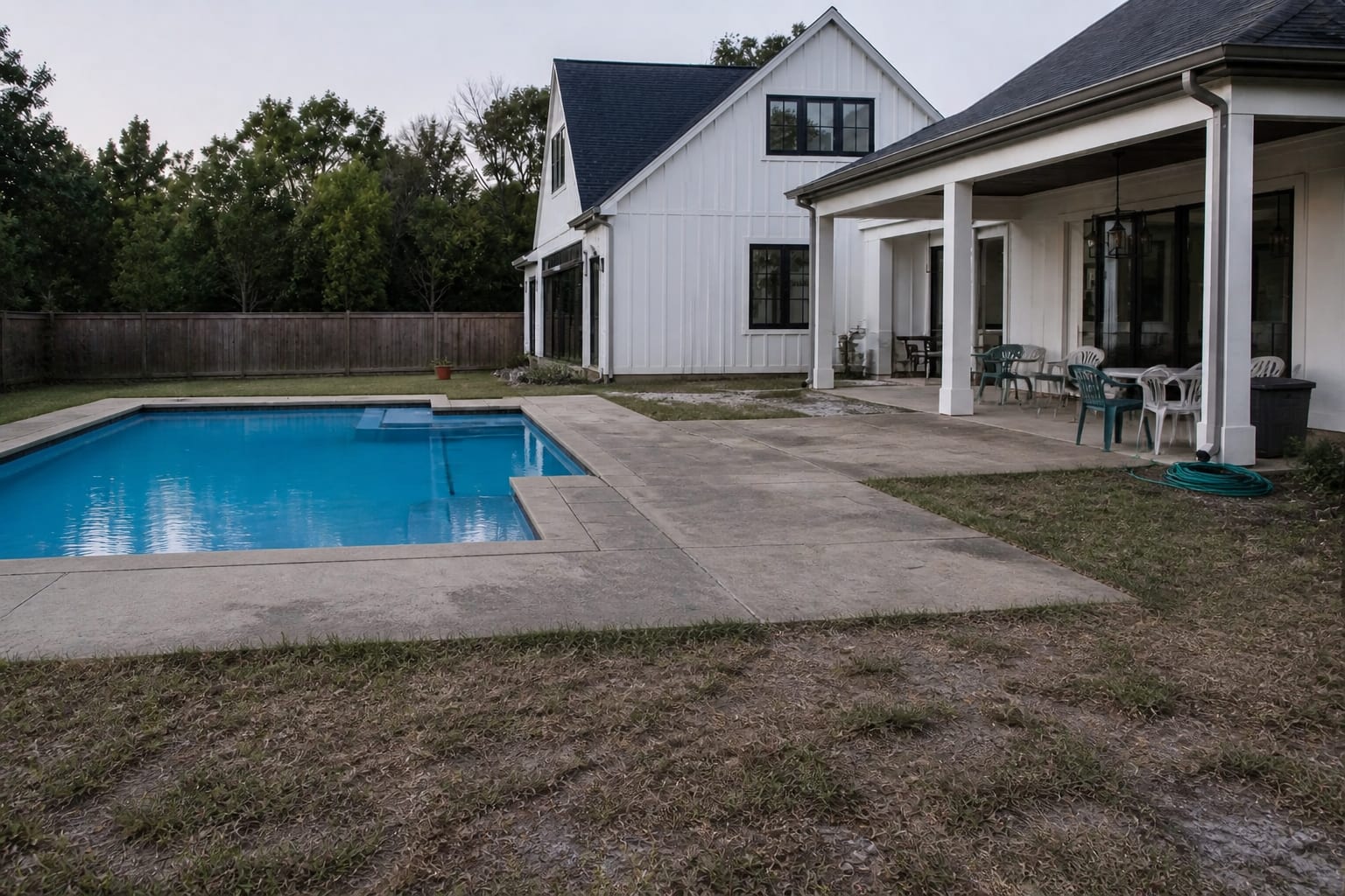 backyard pool with open deck edges, scattered lounge chairs, no clear safety enclosure, and exposed lawn beside the water