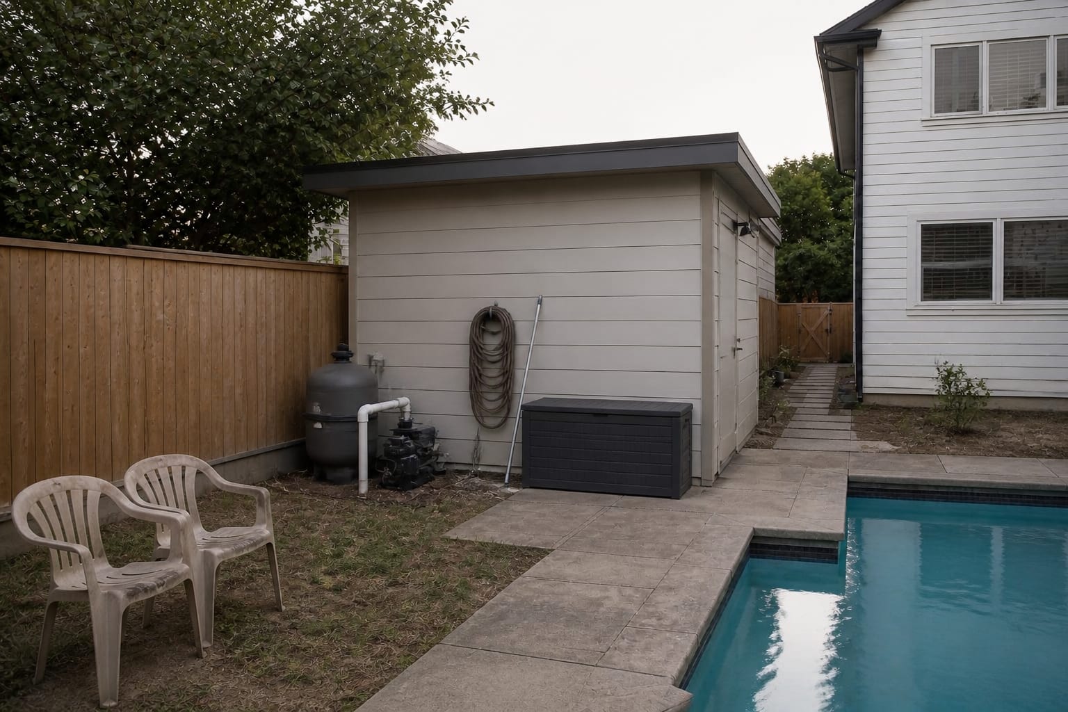 Underused pool corner with exposed fence, scattered towels, no shade, and pool equipment visible from the deck