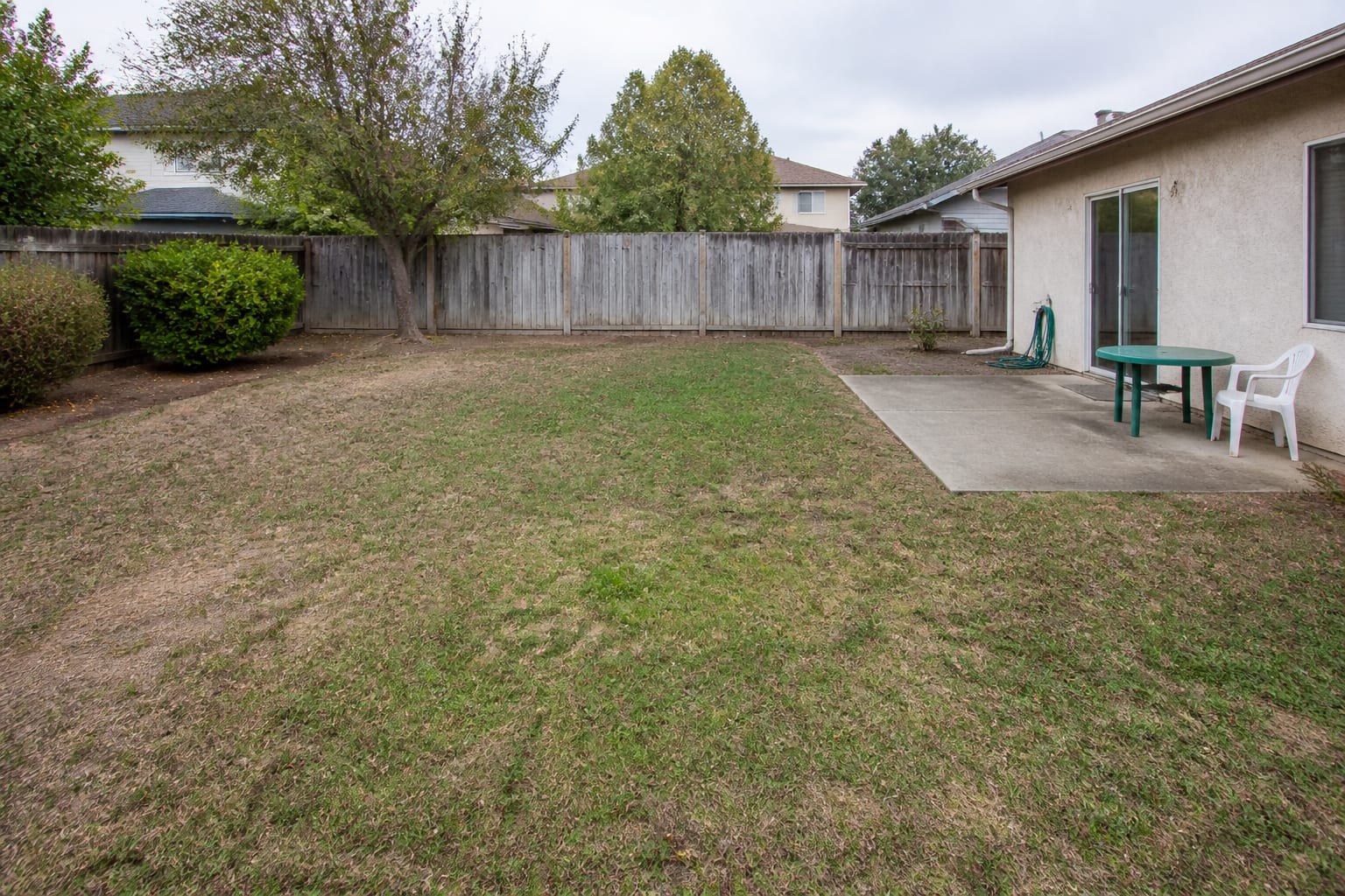 A plain rectangular backyard with patchy lawn and a wood fence before any pool is built