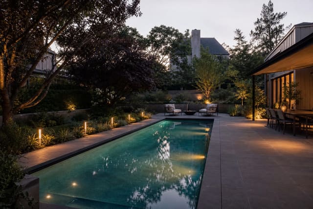 warm modern pool area with underwater lights, low perimeter markers, layered planting, and shielded landscape lighting at dusk