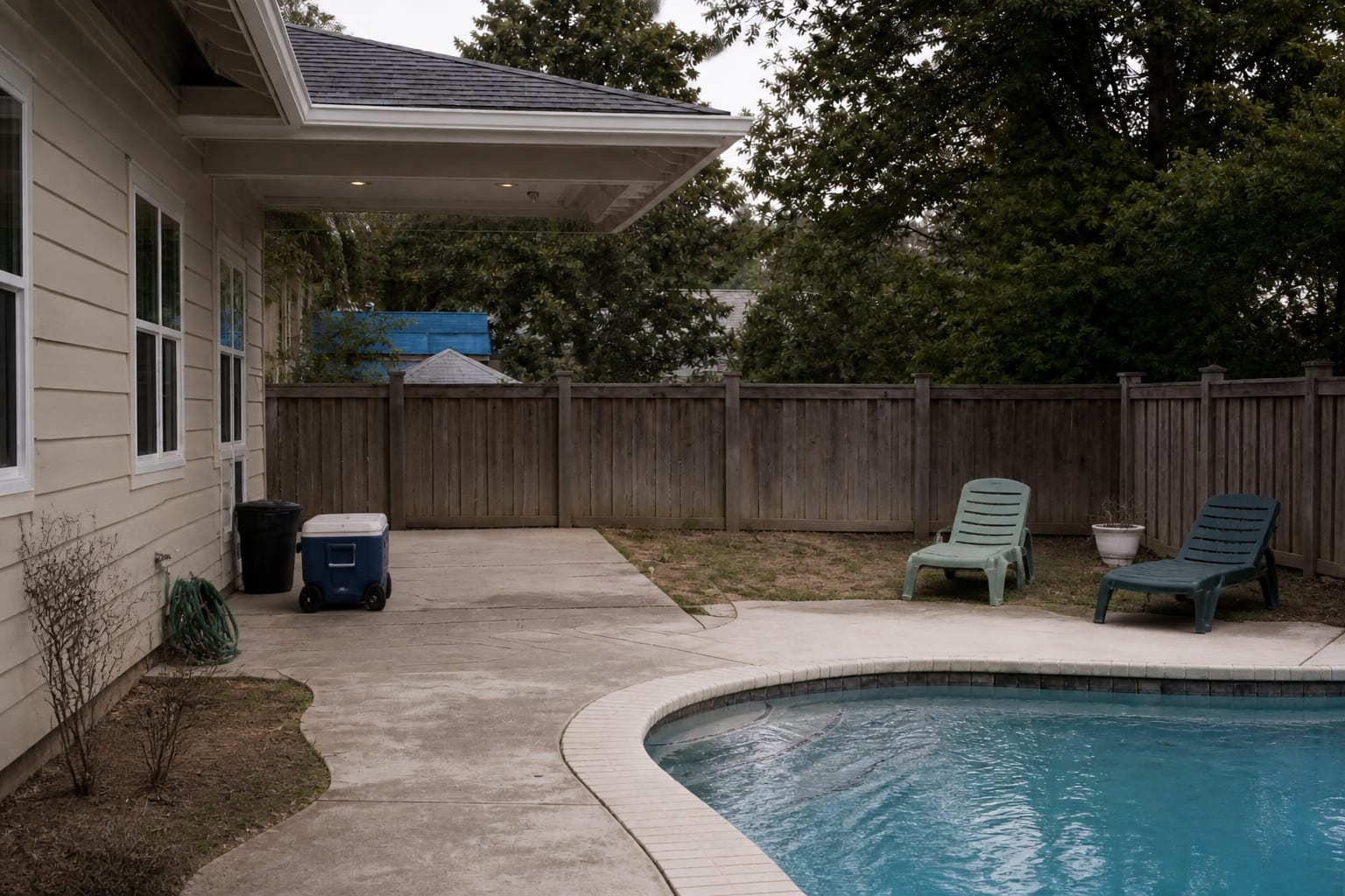 pool patio corner with a plastic cooler, scattered towels, no shade, and lounge chairs blocking the walking path around the water.