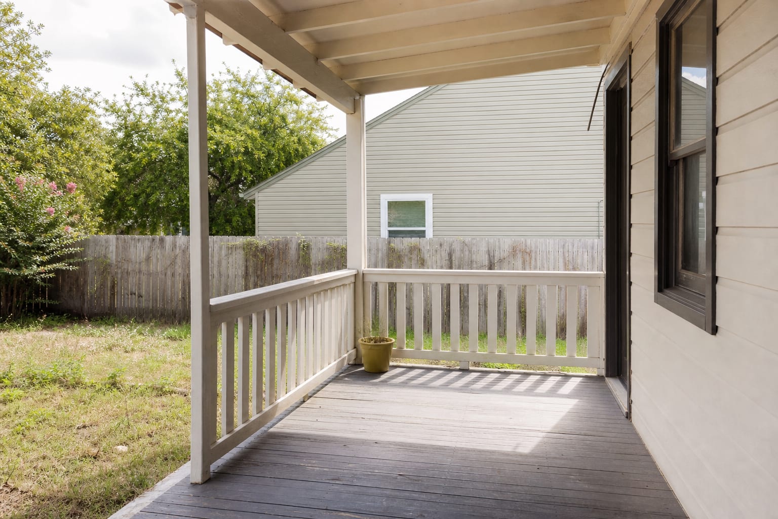 underused porch corner with bare floorboards, no swing, and a single small planter near the railing