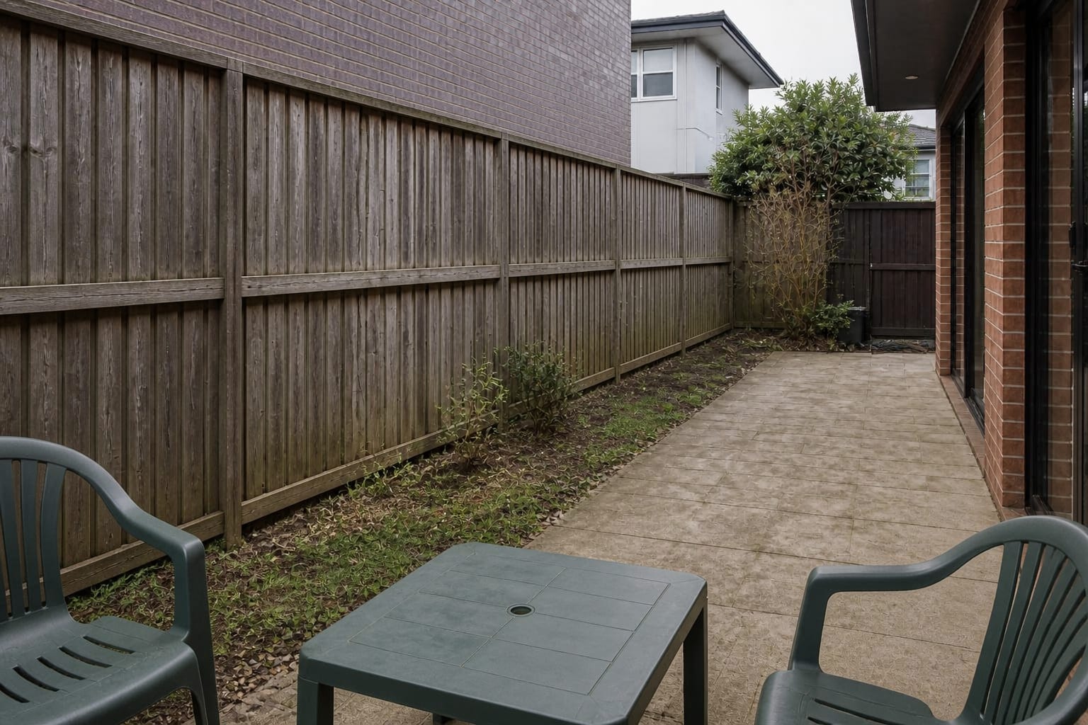 narrow garden patio with exposed fence line, thin planting, visible neighboring window, and no vertical privacy structure.