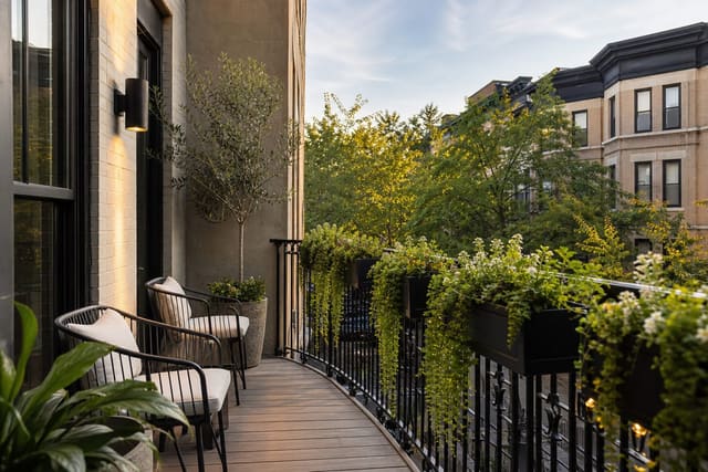 balcony railing with black metal flower boxes, trailing greenery, compact chairs, and a clear walking path on a city balcony