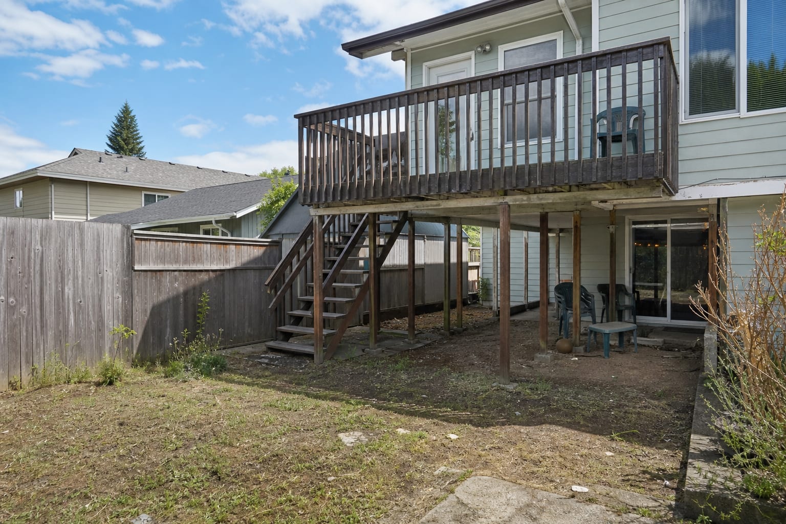 high backyard deck with exposed posts, narrow stairs, bare ground below, and no clear connection between the upper platform and yard.