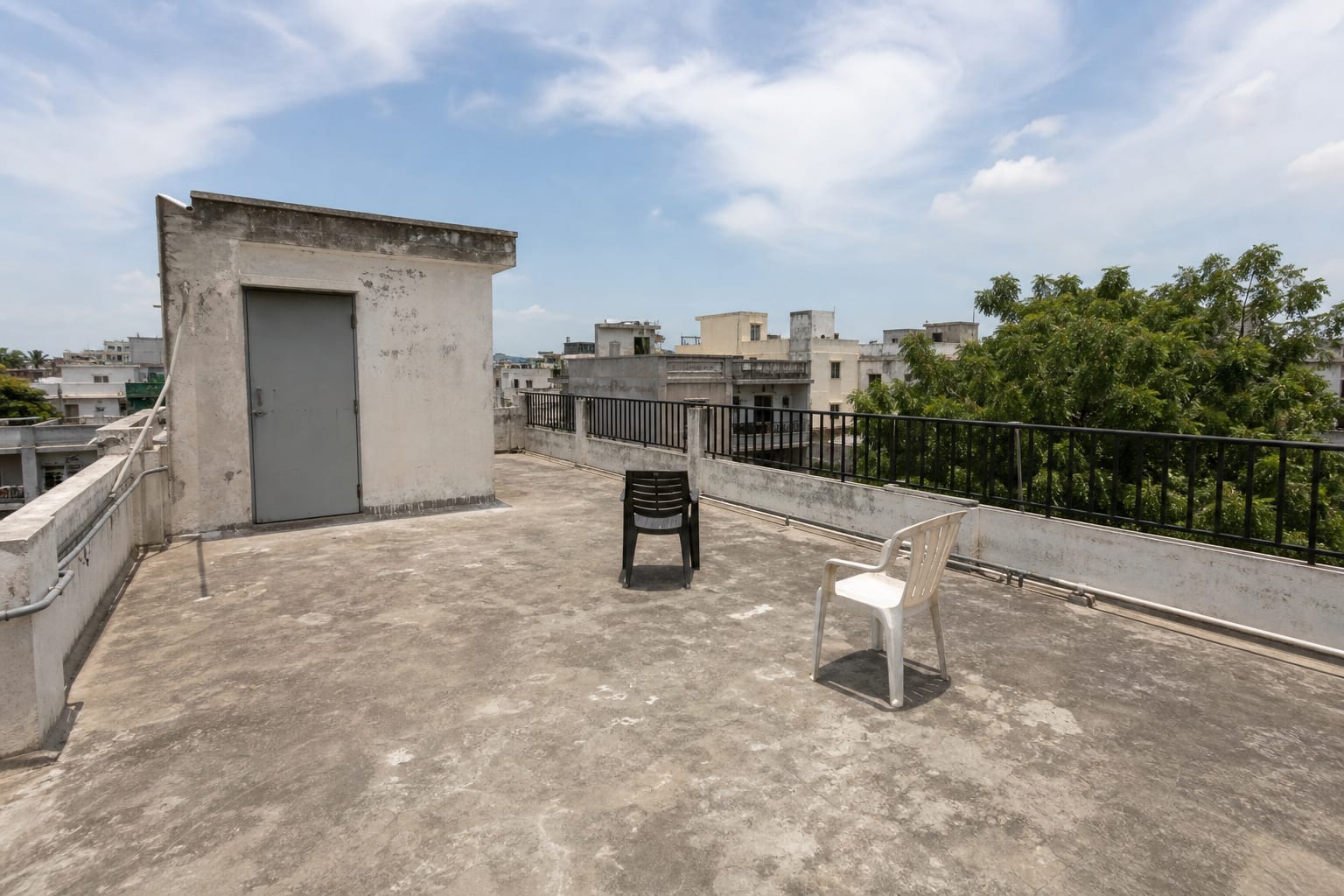 plain rooftop access area with bare waterproofing, exposed railings, scattered chairs, no shade, and no defined seating zone