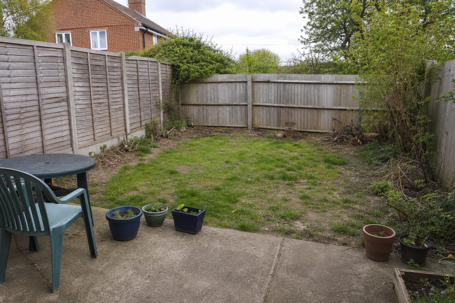 Under designed garden corner with patchy lawn, a plain fence, random pots, no path layout, and no clear place for roses to climb or repeat.