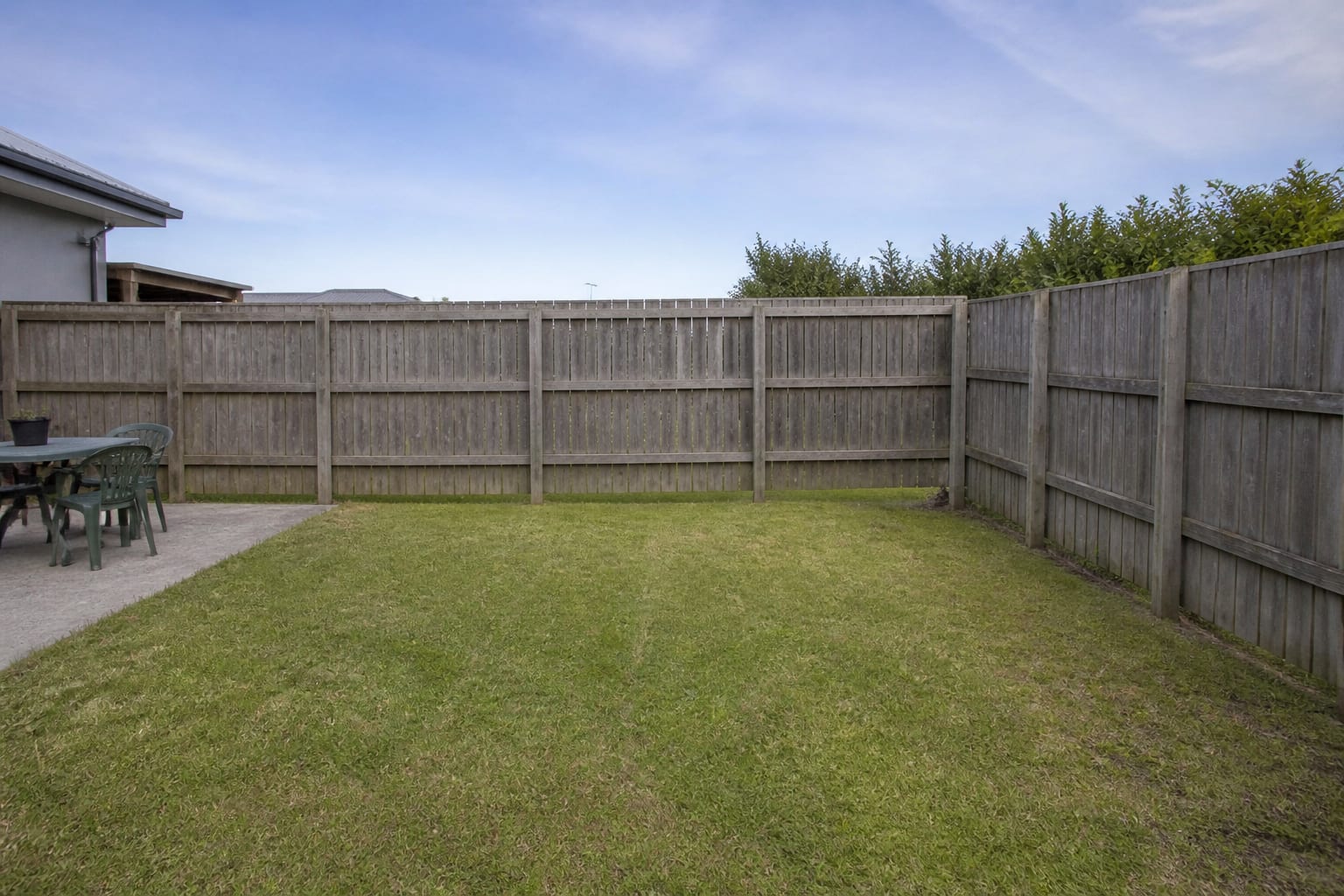 Flat empty lawn corner with a bare fence and no planting before a sensory garden