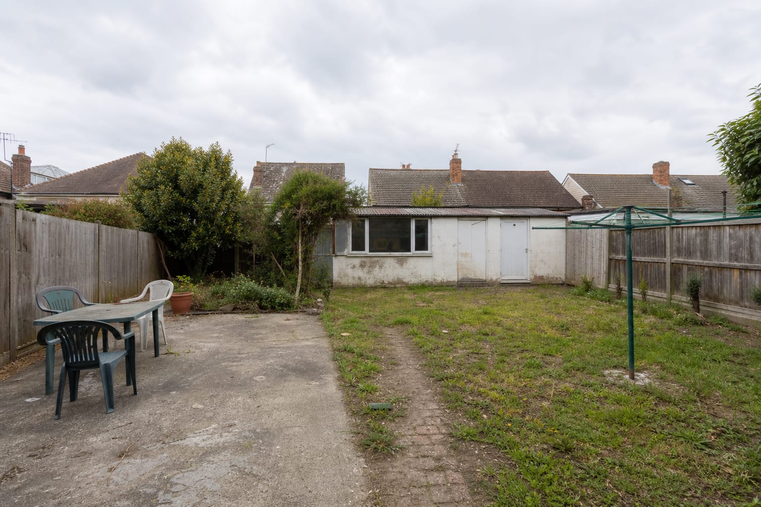 Patchy shaded soil beside a plain fence with sparse grass, exposed roots, and no clear planting structure.