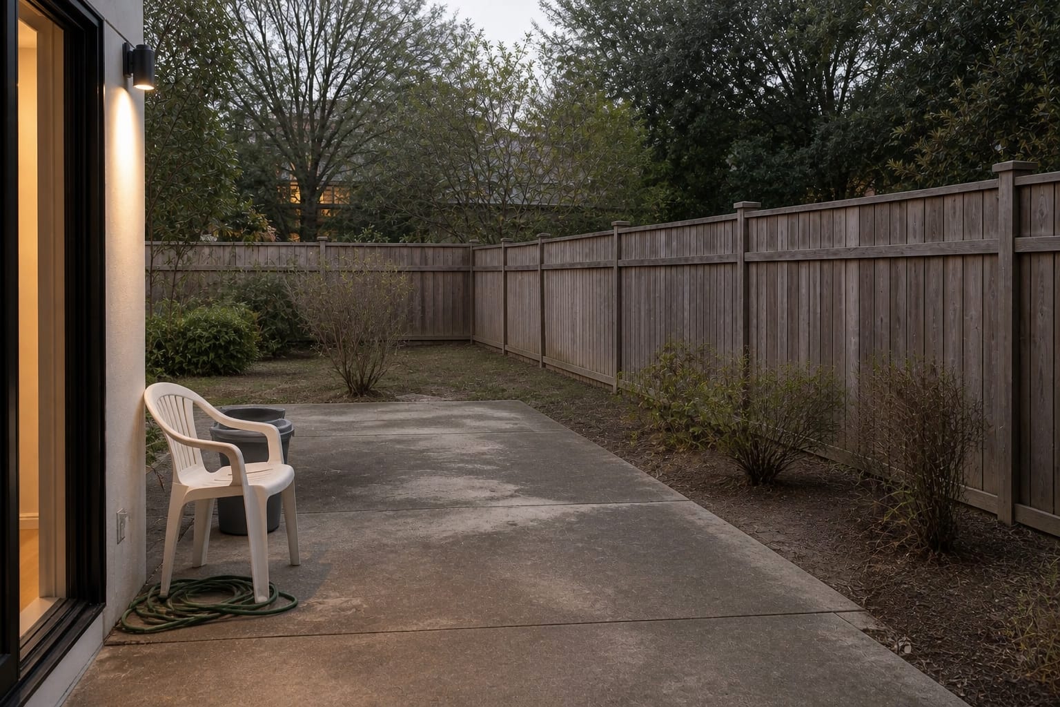 under-designed concrete patio with mismatched chairs, exposed fence line, and no planting structure