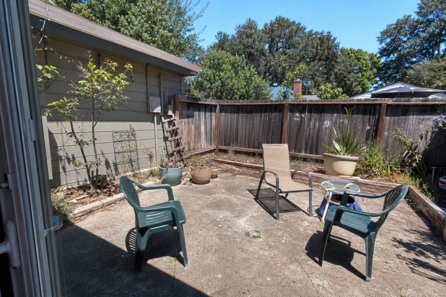 under-designed concrete patio with mismatched chairs, exposed fence line, and no planting structure