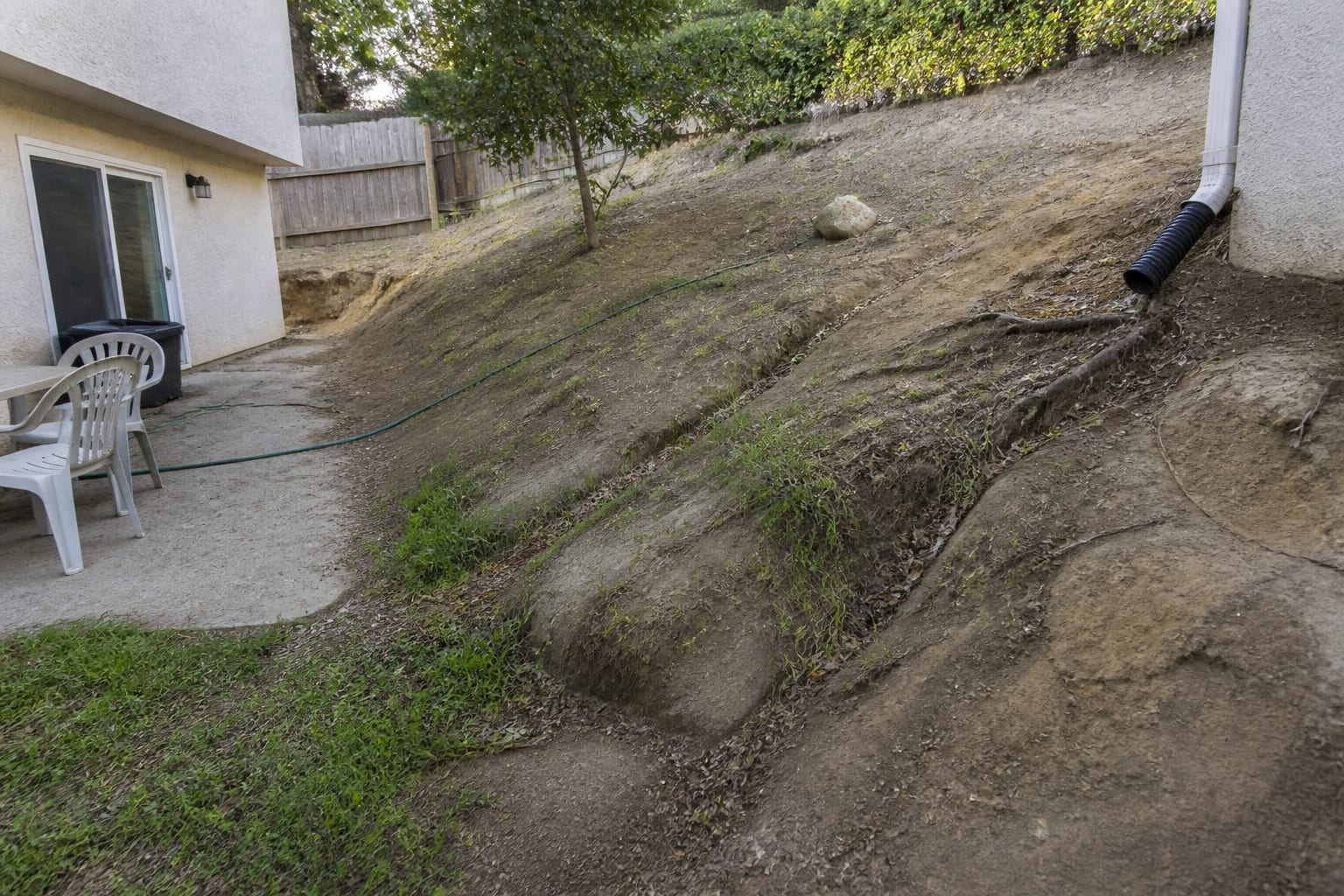 Eroding bare dirt slope with washed-out gullies and patchy dead grass before landscape redesign