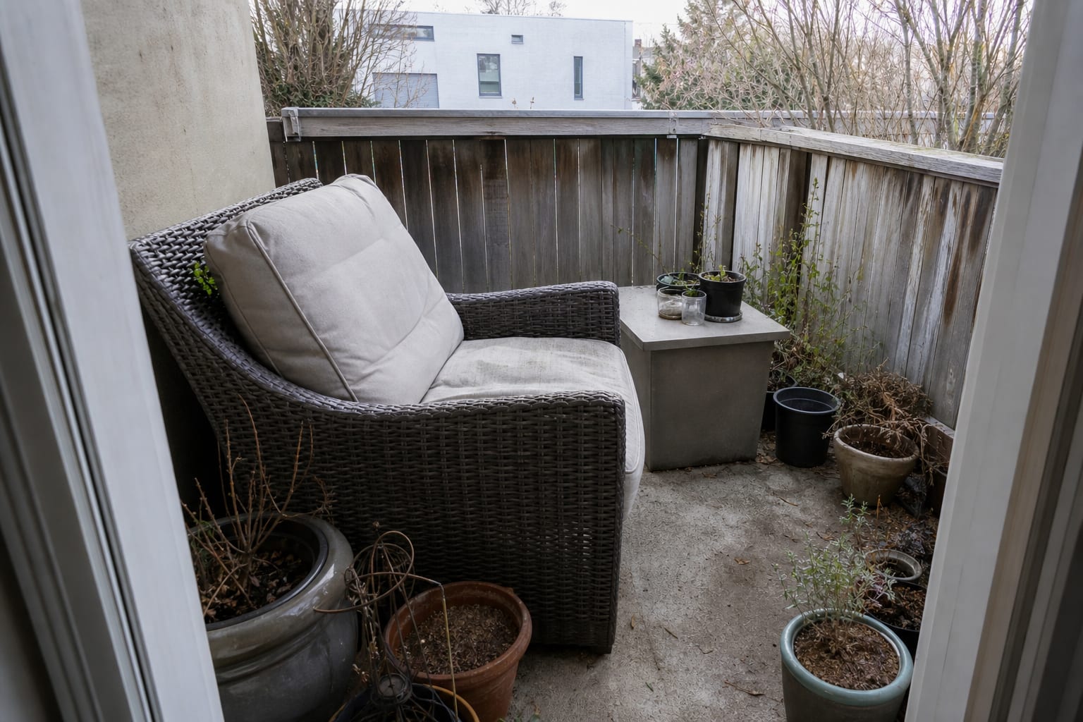Narrow apartment balcony with an oversized outdoor chair blocking the door and loose pots crowding the walking path.
