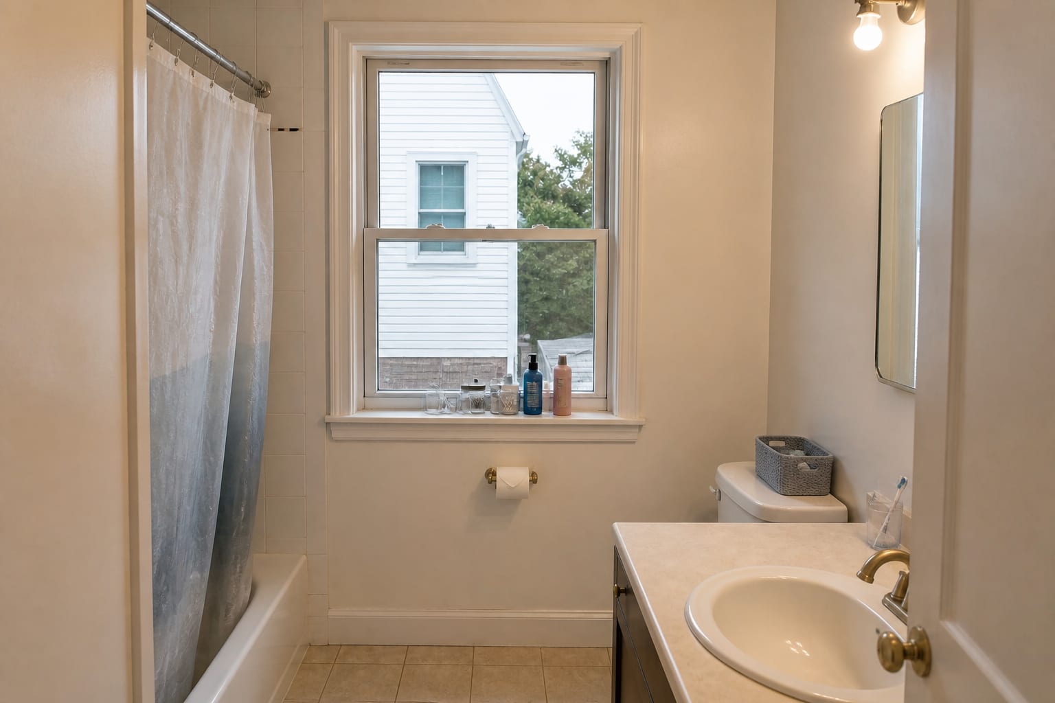 Small bathroom with a bare double-hung window, exposed lower sash, cluttered sill, and harsh overhead light.