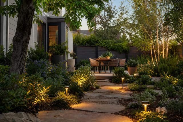 warm solar path lights leading through a planted garden toward a small patio with soft low-level lighting